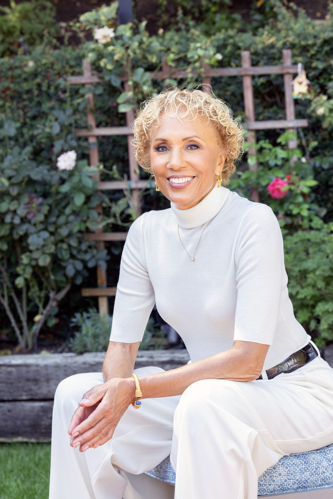Deborah Santana smiling outside, elbows on thighs